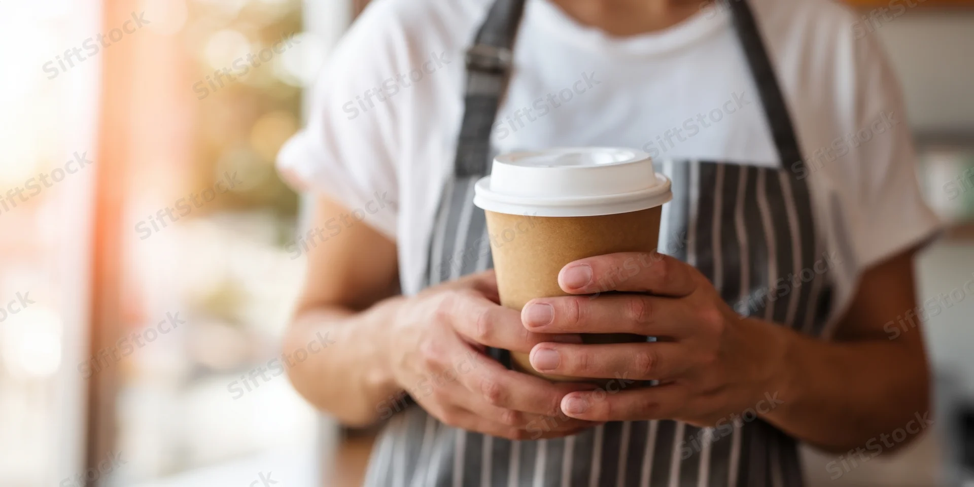 Barista holding a brown disposable coffee cup in a cafe interior