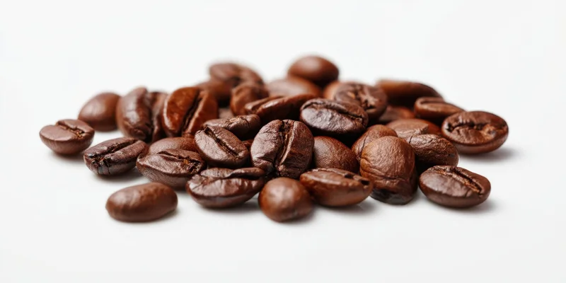 Roasted coffee beans scattered in a pile on a white surface