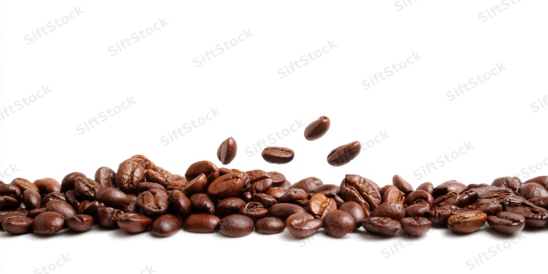 Roasted coffee beans scattered in a line with some falling mid-air on white background
