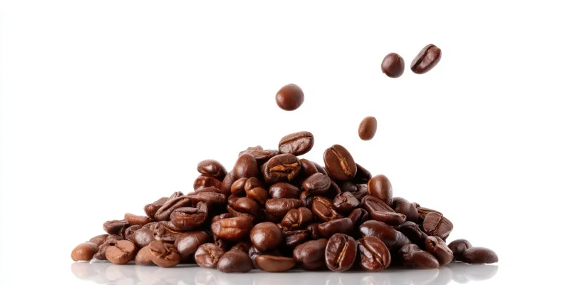 Roasted coffee beans piled on white surface with some falling into the heap