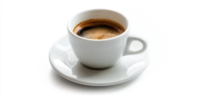 White ceramic coffee cup with espresso crema on matching saucer isolated on white background