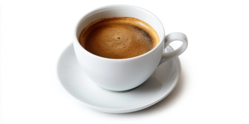 White ceramic coffee cup with espresso crema on matching saucer isolated on white background