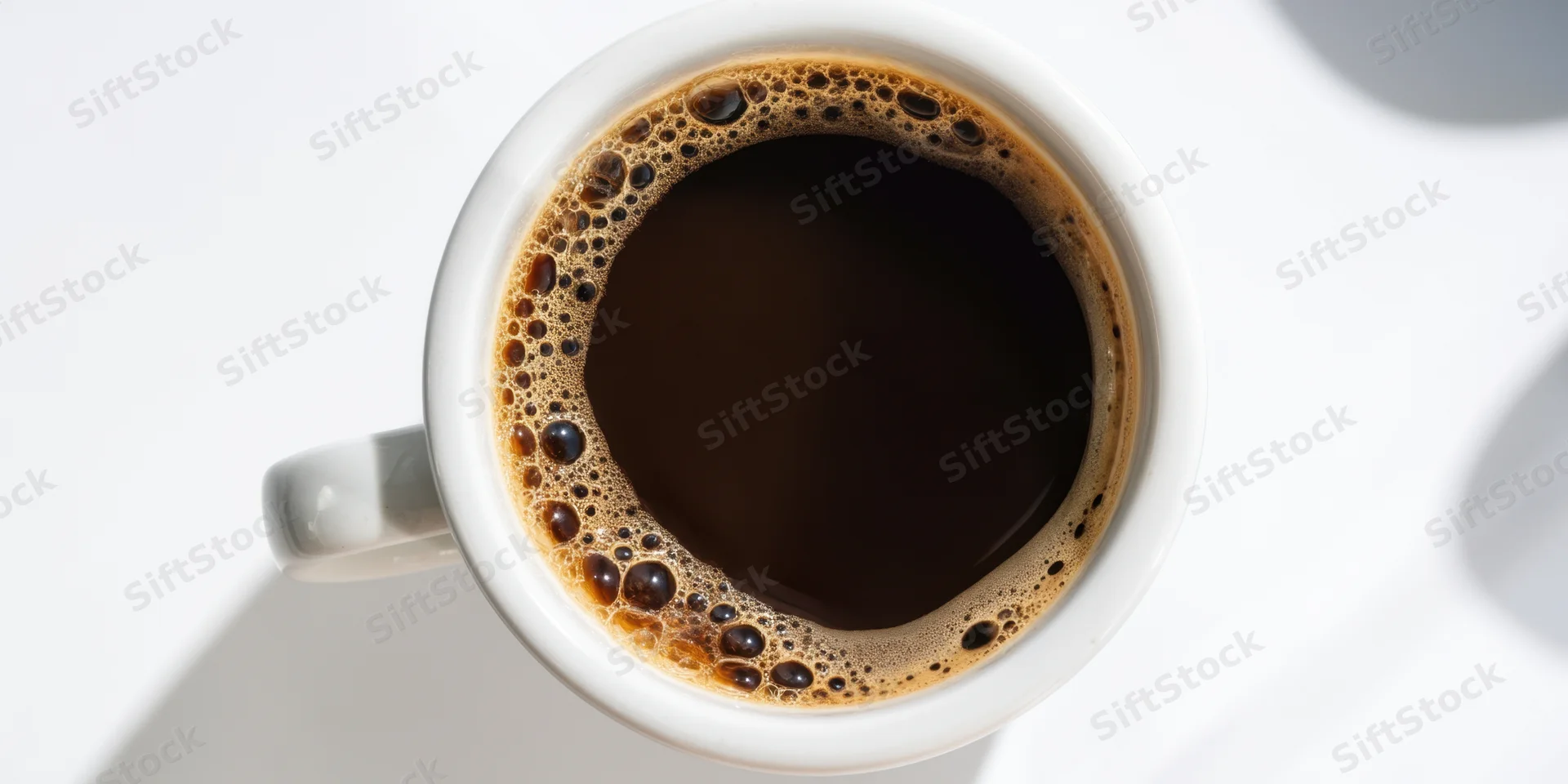 Top-down view of a white ceramic cup filled with dark coffee on a white surface