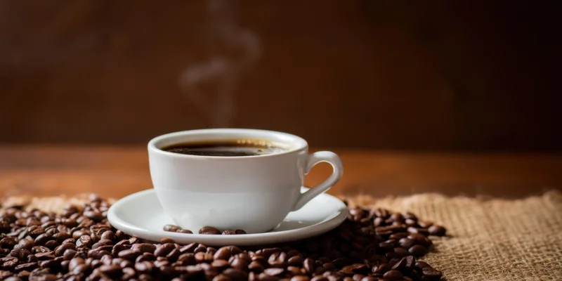 Steaming coffee cup on saucer surrounded by roasted beans on burlap surface