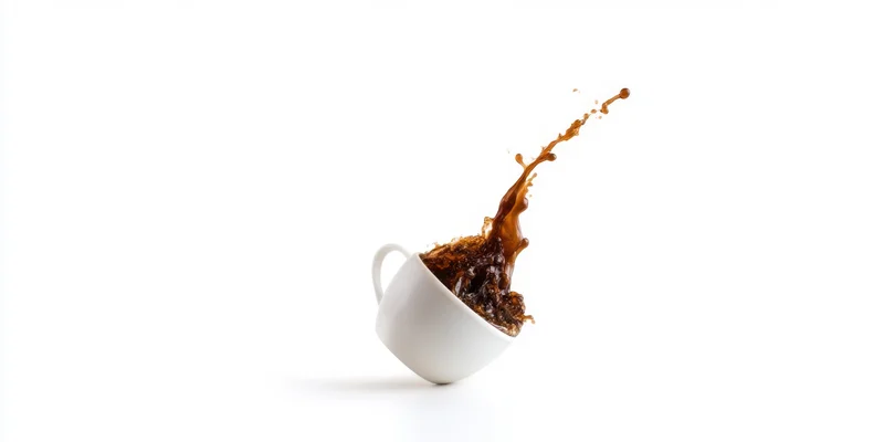 White ceramic coffee cup tilting with dark coffee splashing upward against white background