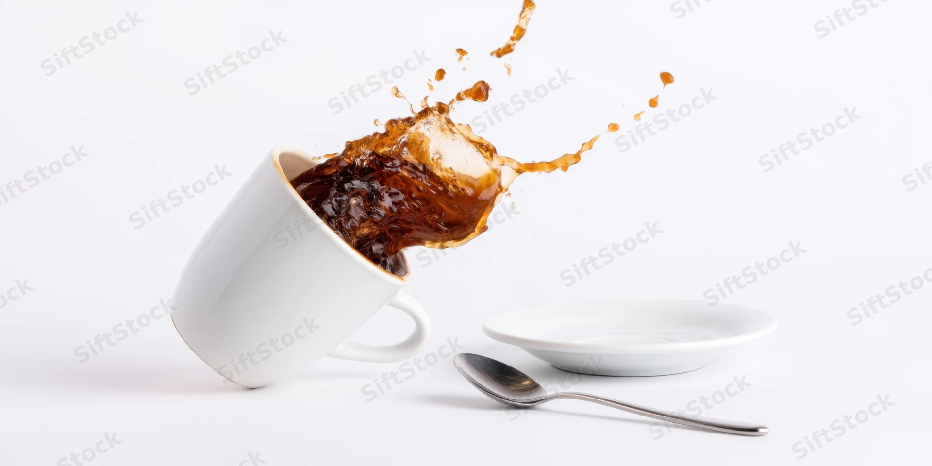 White ceramic coffee cup tilting with espresso splashing out against white background