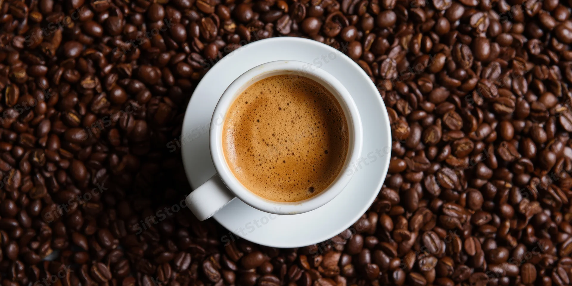 White ceramic coffee cup with crema on saucer surrounded by roasted coffee beans, top view