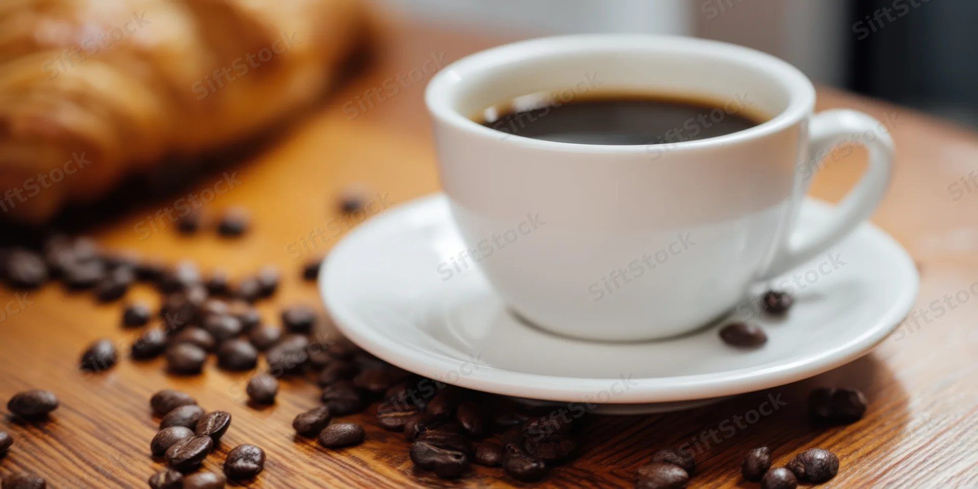 White ceramic coffee cup on saucer with scattered beans on wooden table