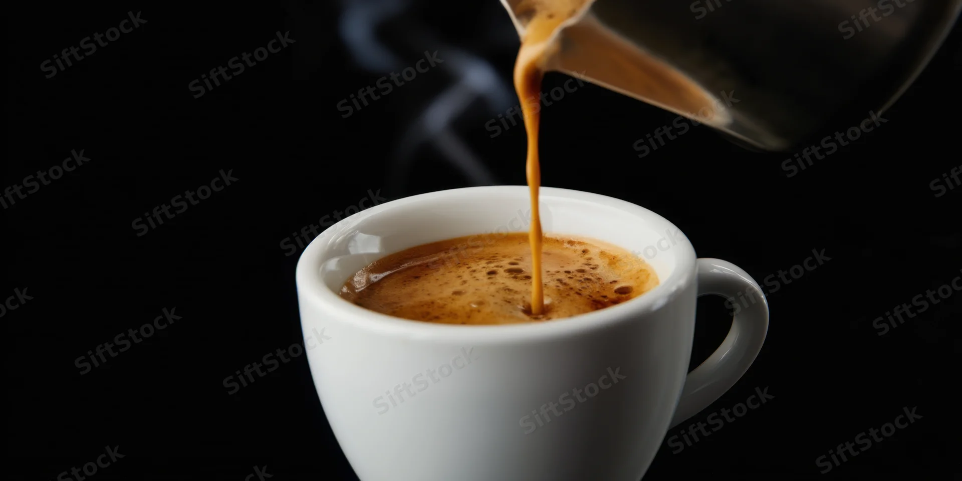 Coffee being poured into a white ceramic espresso cup with crema and steam against a black background