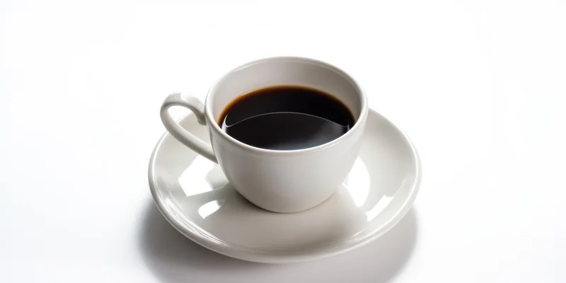 White porcelain coffee cup filled with dark coffee on saucer against white background