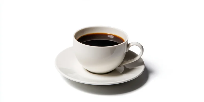 White porcelain coffee cup filled with dark coffee on saucer against white background