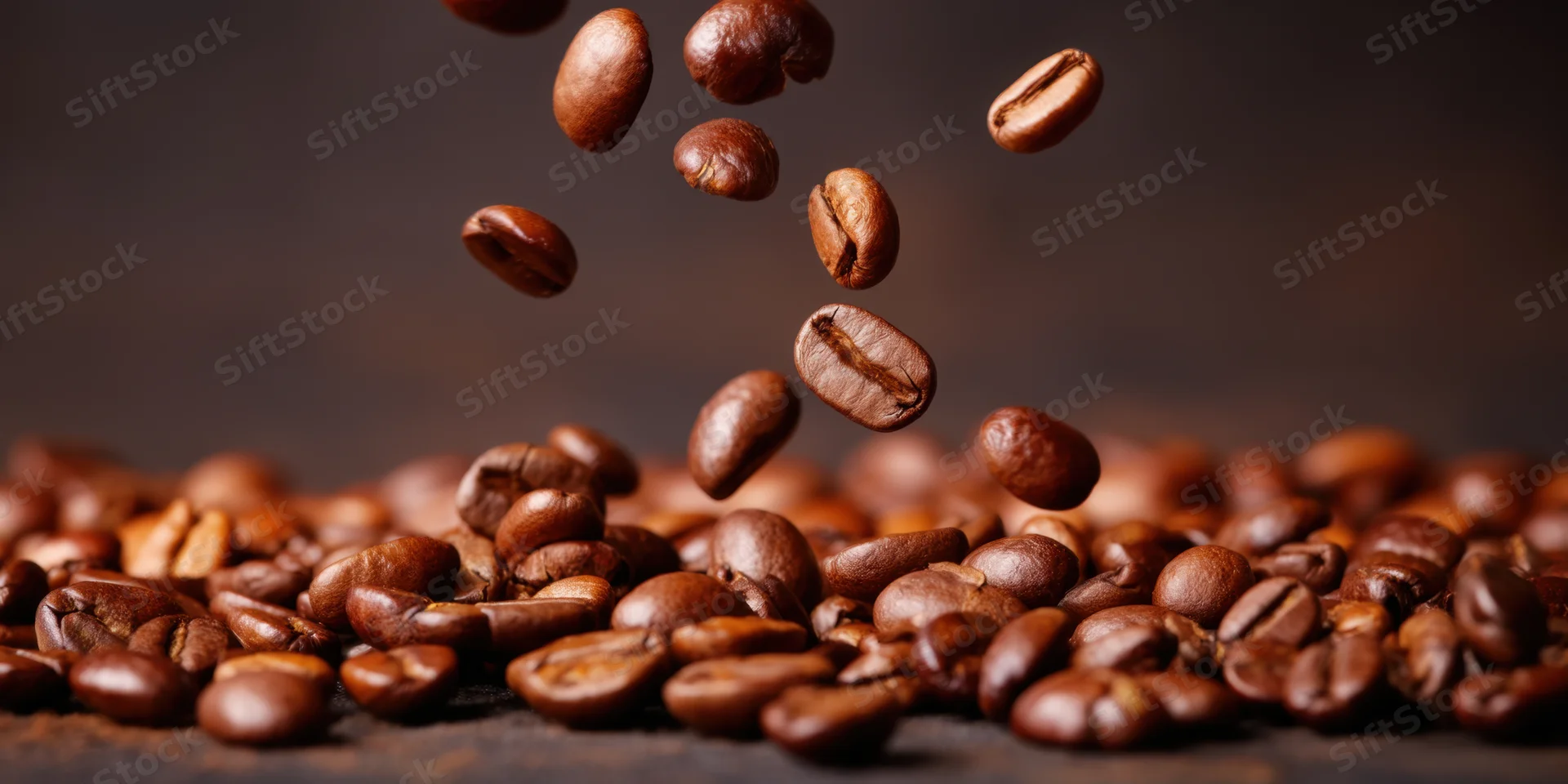 Roasted coffee beans falling in midair onto a pile on a dark surface
