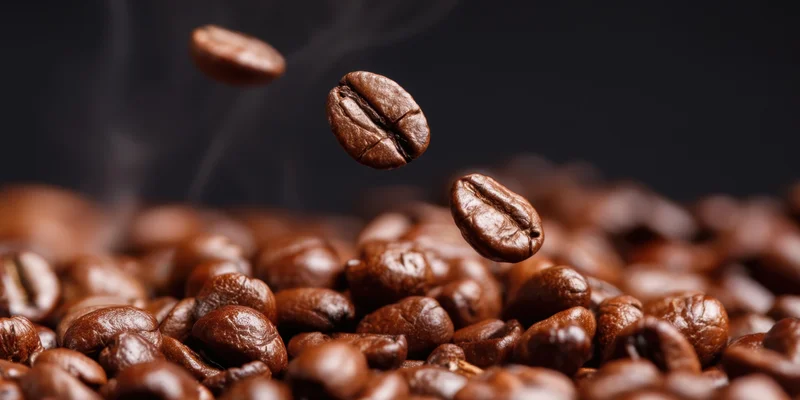 Roasted coffee beans falling in midair above a pile with steam rising against dark background