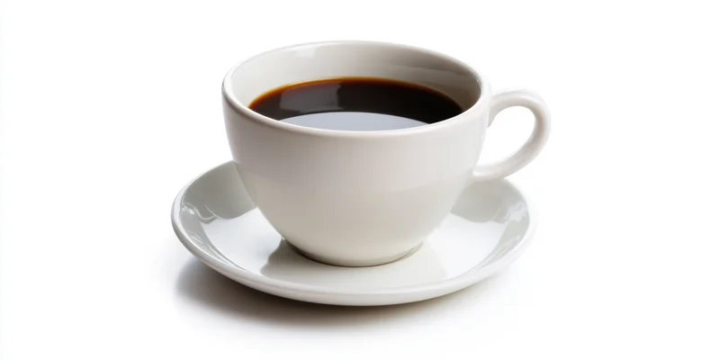 White ceramic coffee cup filled with dark coffee on matching saucer against white background