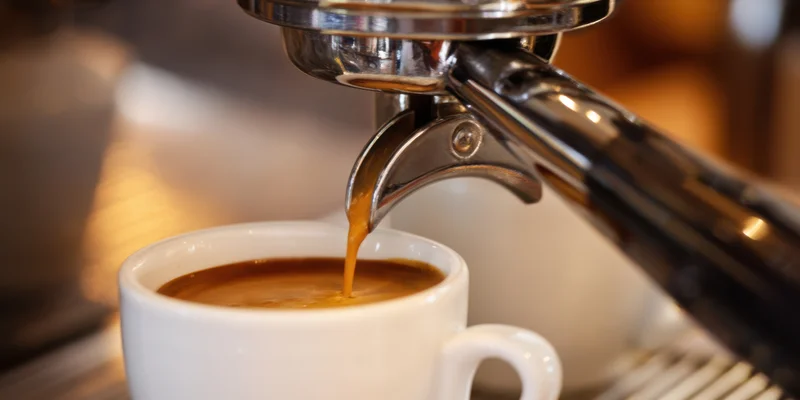 Espresso machine pouring coffee into a white cup on a cafe counter
