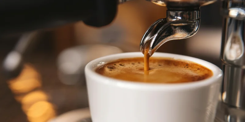 Espresso pouring from machine into white cup in café setting