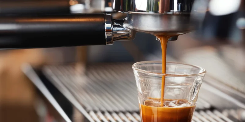 Espresso pouring from a machine into a clear glass cup on a metal counter