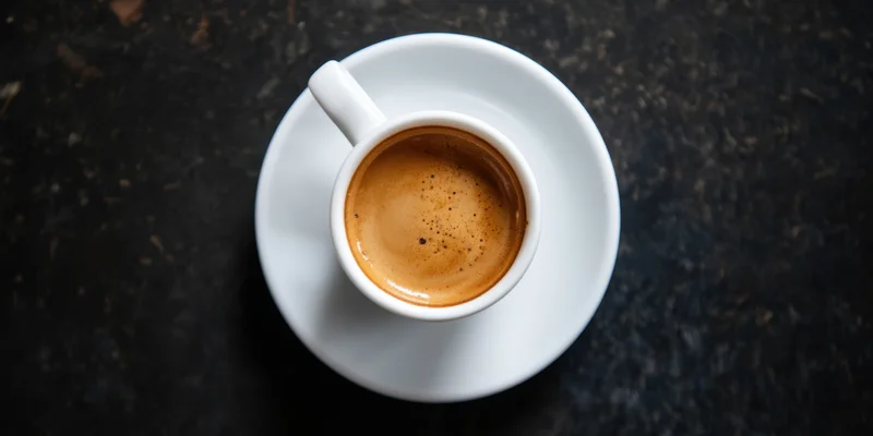 White porcelain espresso cup with crema on dark surface, top-down view