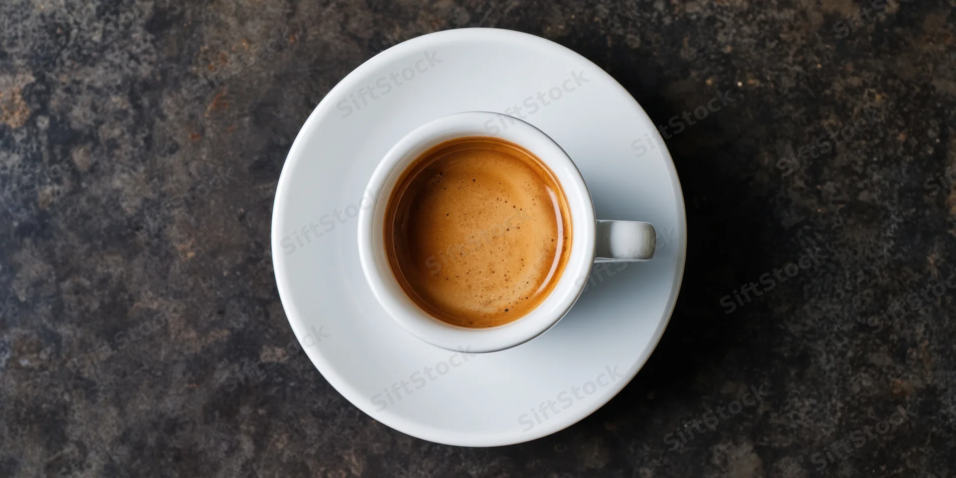 Top-down view of a white porcelain espresso cup with crema on a dark textured surface