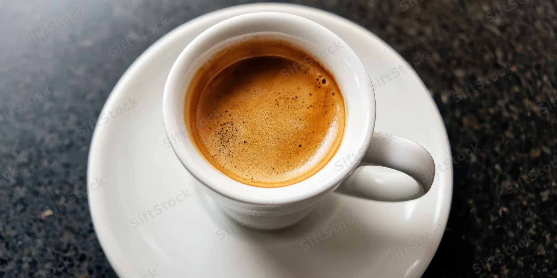 White porcelain espresso cup with crema on saucer on dark countertop, top-down view