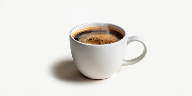 White ceramic mug filled with steaming dark coffee on plain white surface
