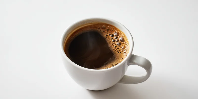 White ceramic mug filled with steaming dark coffee and crema on plain white surface