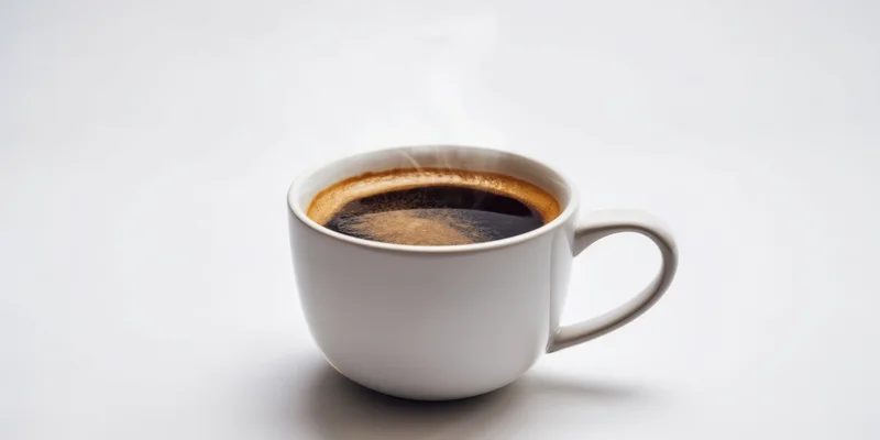White ceramic mug filled with steaming dark coffee on plain white surface