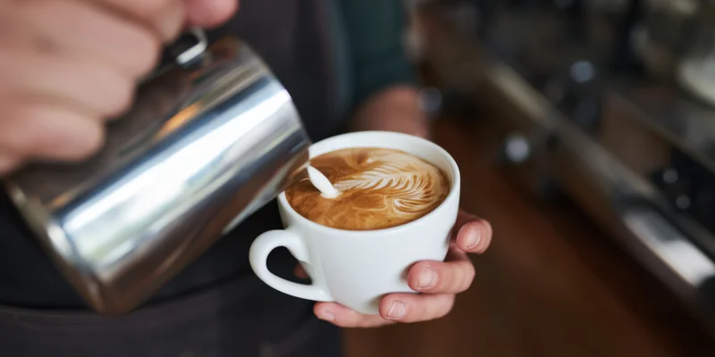Barista pouring steamed milk into a white cup to create latte art in a coffee shop