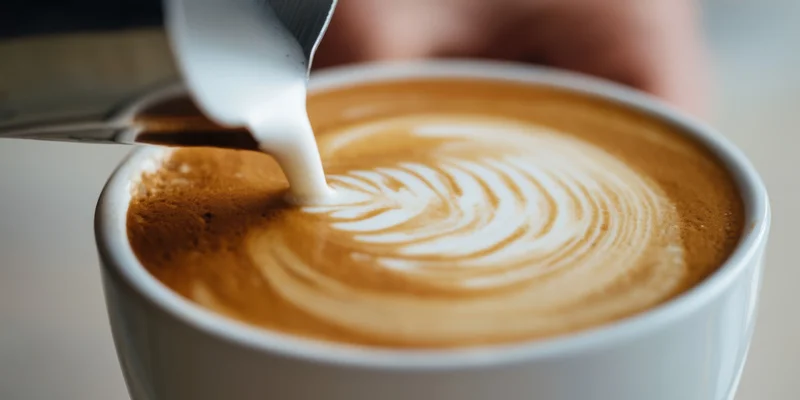 Barista pouring microfoam into a latte cup to create latte art in a coffee shop