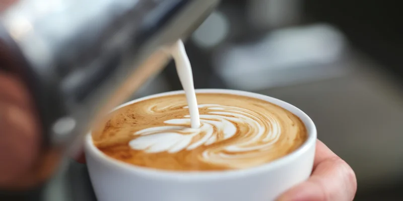 Hand pouring microfoam into a latte cup to create latte art in a coffee shop