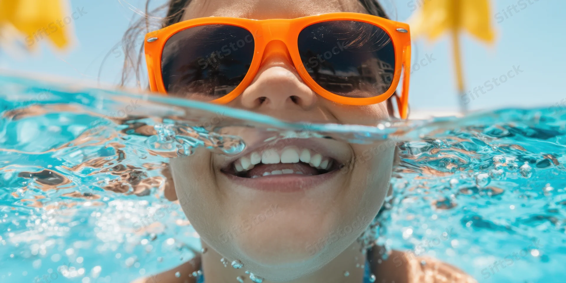 Child smiling with orange sunglasses half-submerged in pool water