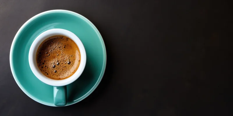 Overhead view of a teal ceramic coffee cup with foam on a matching saucer on a dark surface