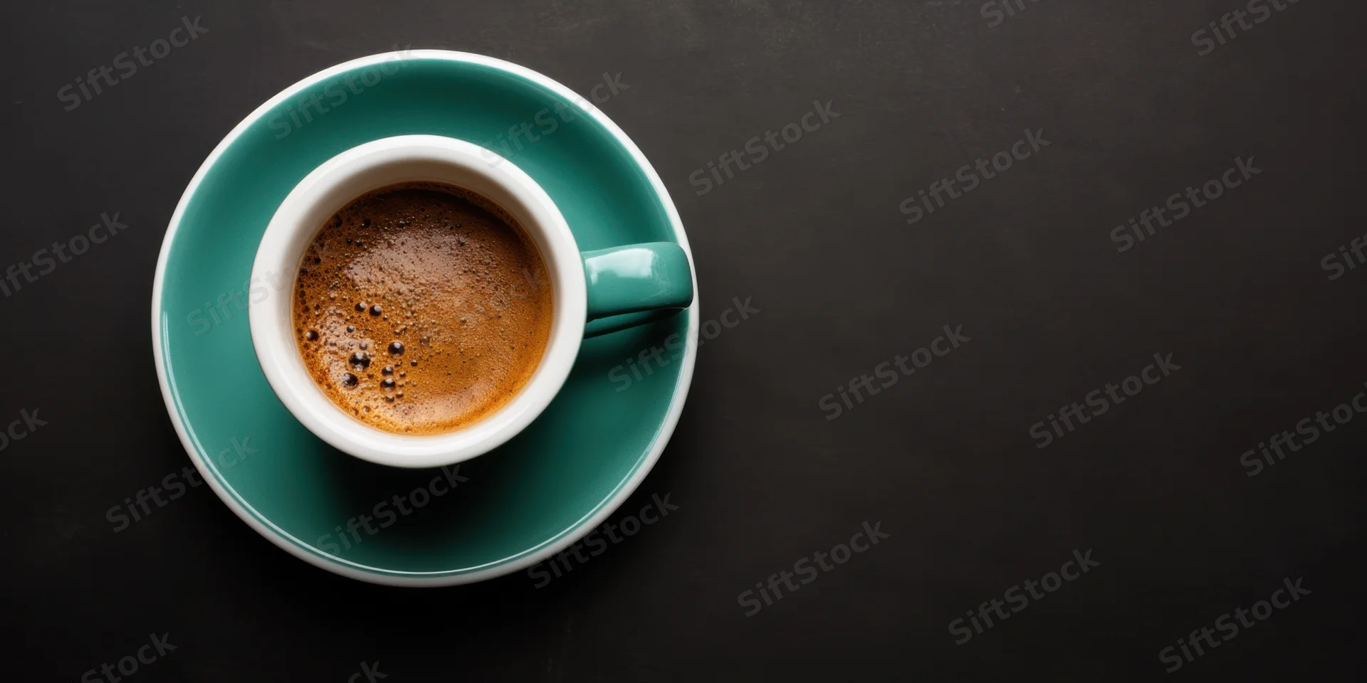 Teal ceramic coffee cup with espresso foam on matching saucer on dark surface, overhead view