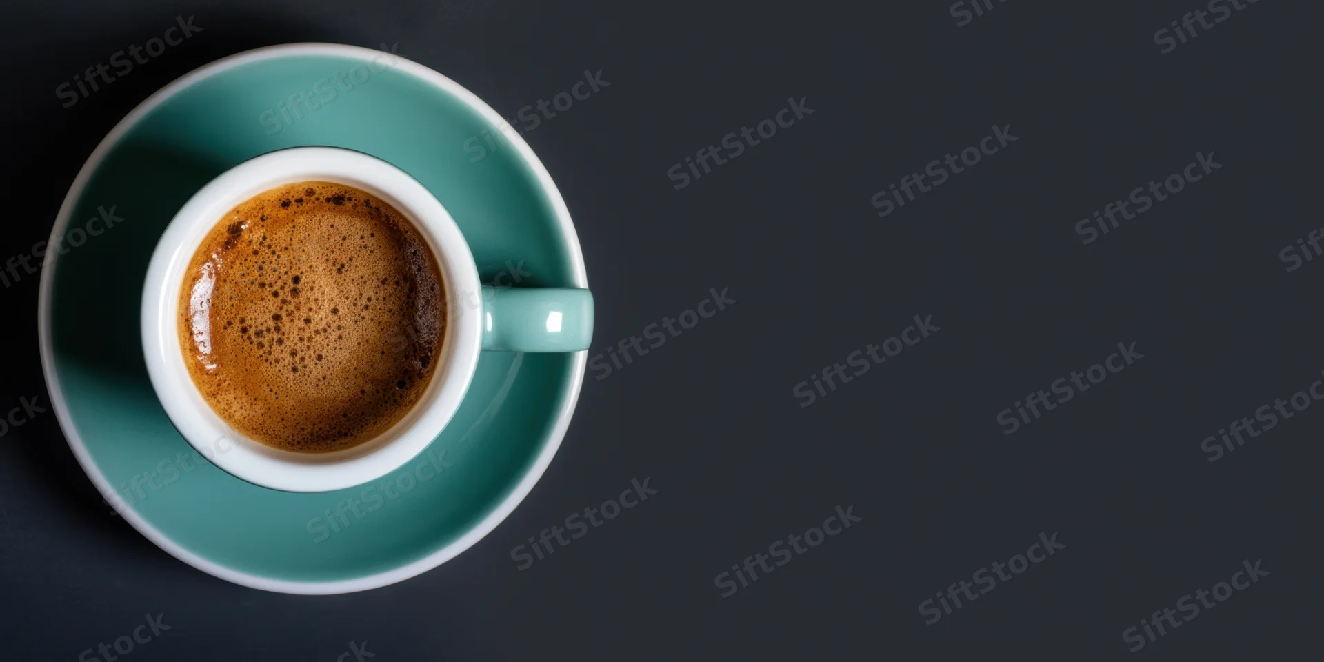 Teal ceramic coffee cup with foam on matching saucer on dark surface, overhead view