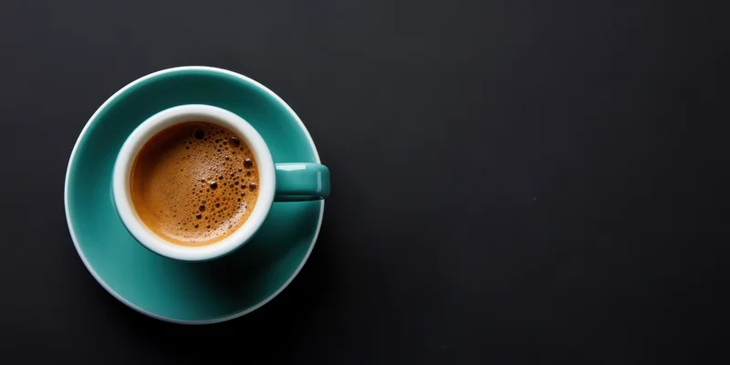 Teal ceramic coffee cup with foam on matching saucer on dark surface viewed from above