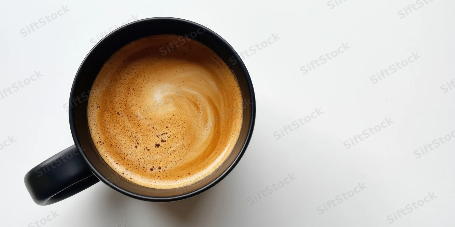Black ceramic mug filled with coffee crema viewed from above on white surface