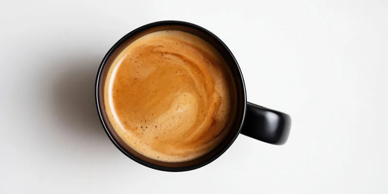 Top-down view of a black ceramic mug filled with coffee crema on a white surface