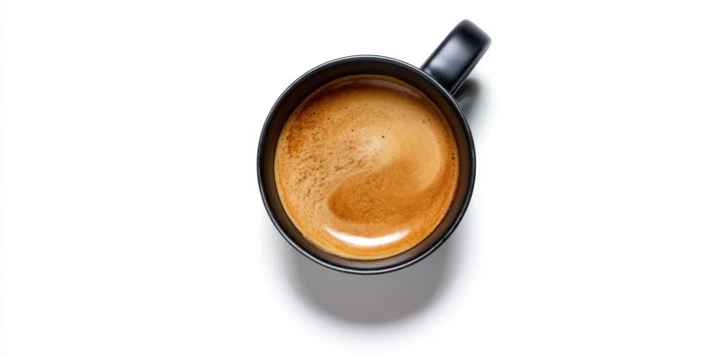 Black ceramic mug filled with coffee crema viewed from above on white background
