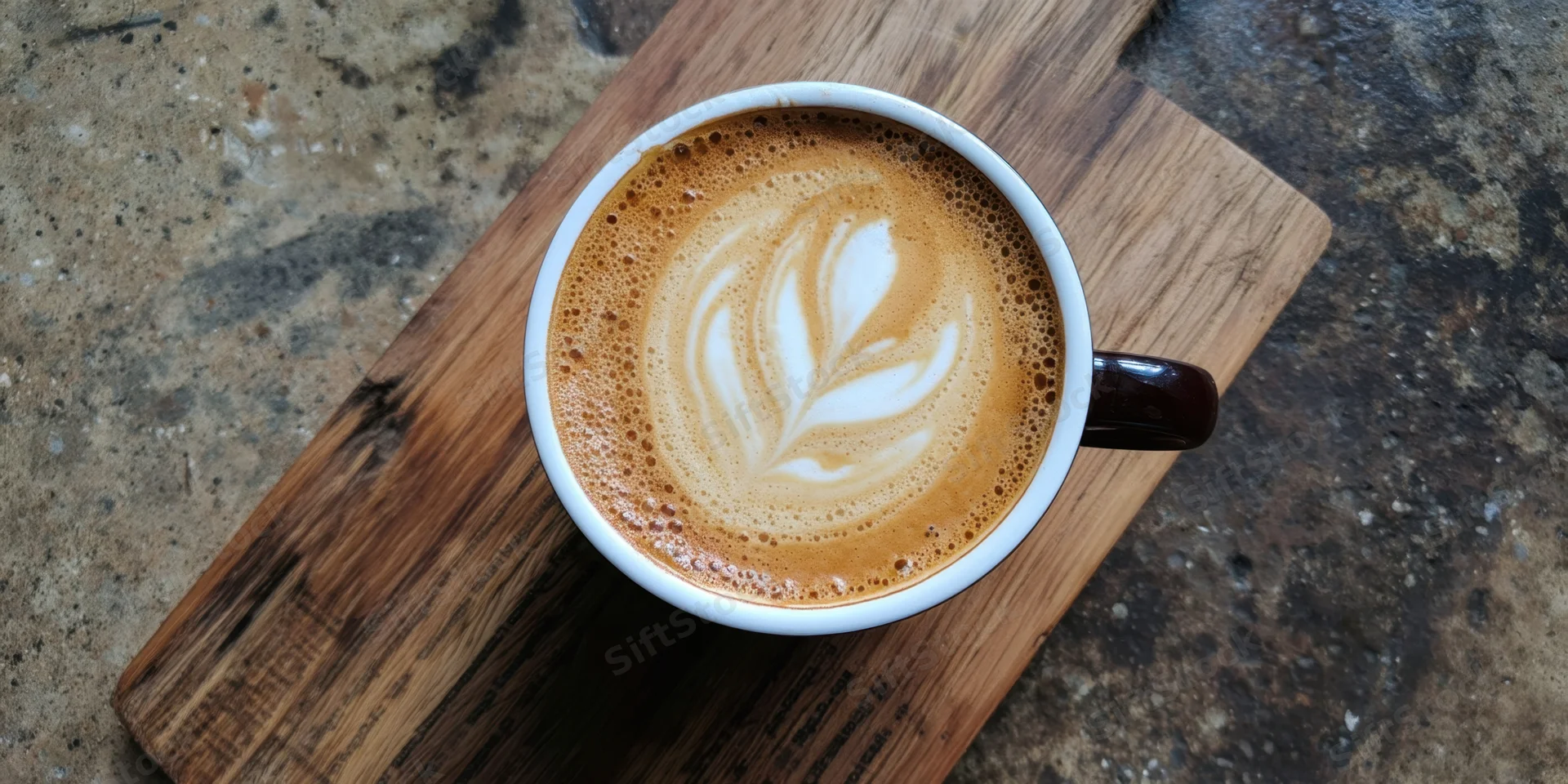 Latte with leaf-shaped foam art in a white ceramic cup on a wooden board