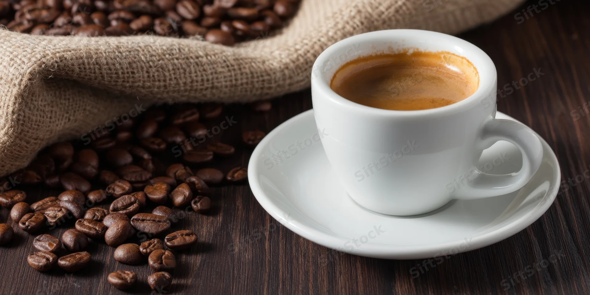 White ceramic espresso cup with crema on saucer beside scattered coffee beans on dark wooden table