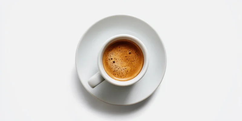 White porcelain espresso cup with rich crema on saucer, overhead view against white background