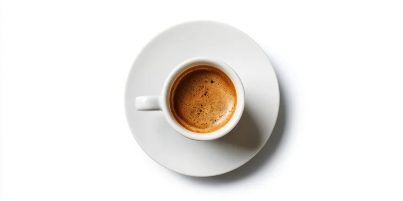 White porcelain espresso cup with rich crema on saucer, overhead view, isolated on white background