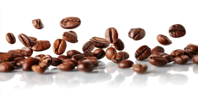 Roasted coffee beans suspended and scattered in midair against a white reflective surface