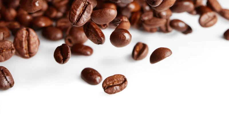 Roasted coffee beans falling and scattered across a white surface