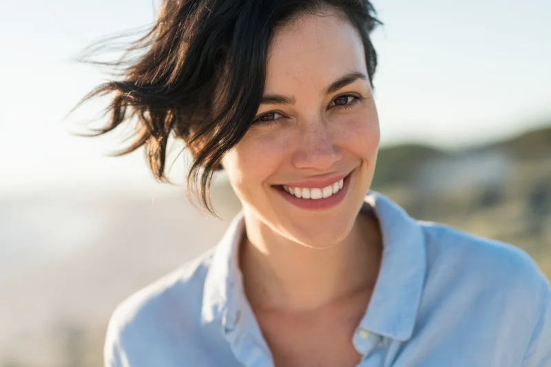 Smiling woman with short dark hair in wind outdoors wearing light blue shirt