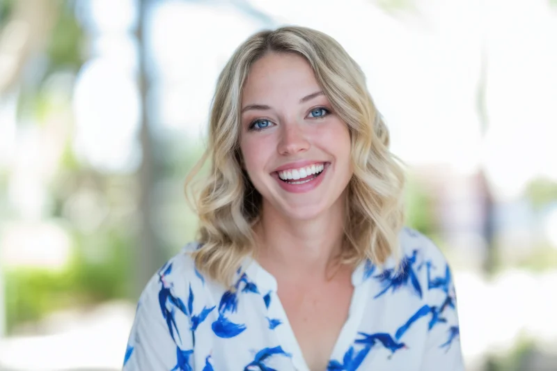 Smiling blonde woman in white blouse with blue bird pattern outdoors in natural light