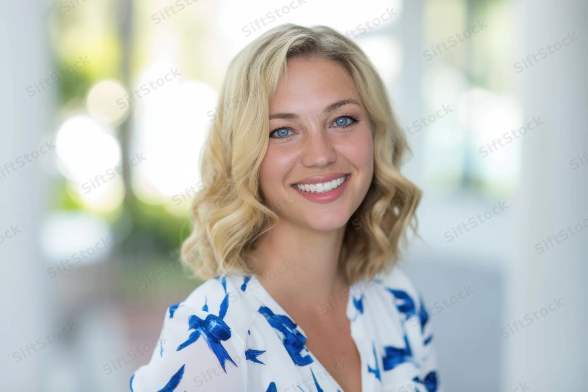 Smiling blonde woman in white floral blouse indoors with bright natural light
