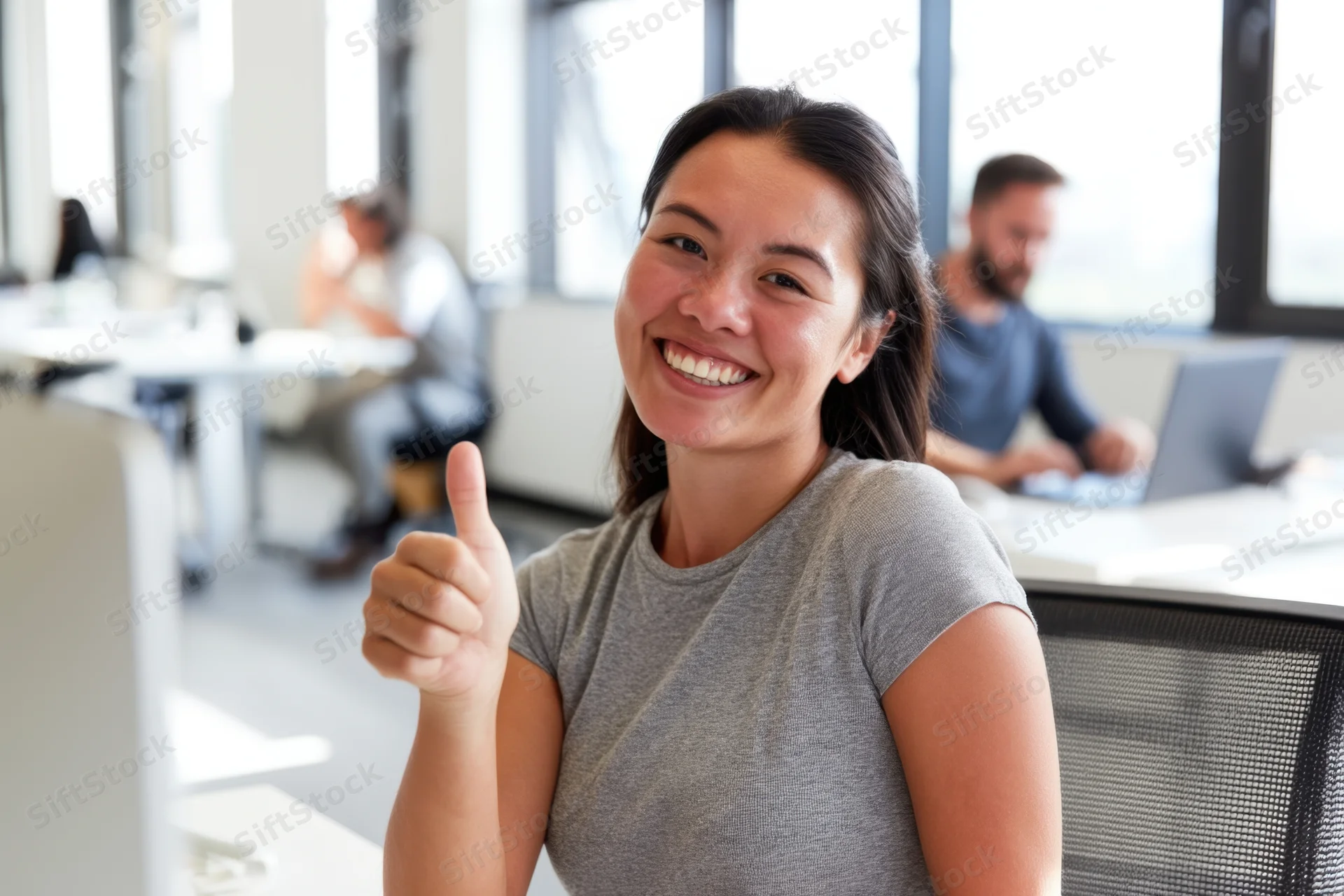 Woman smiling and giving thumbs up at office desk