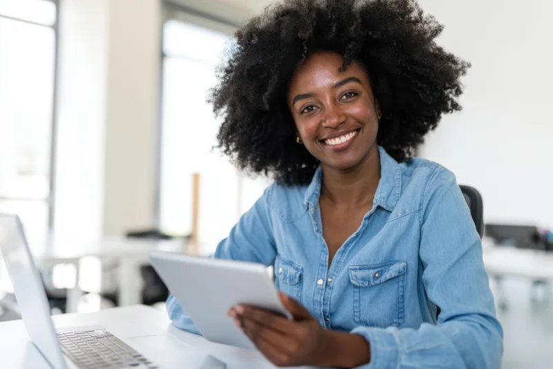 Woman with afro smiling while holding tablet at office desk