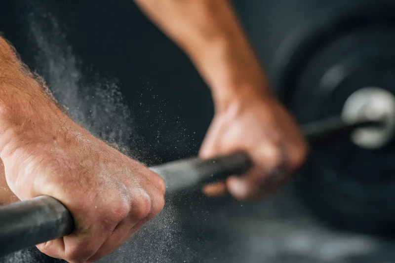 Close-up of a muscular man's hands gripping a barbell with chalk dust flying during a weightlifting workout in the gym